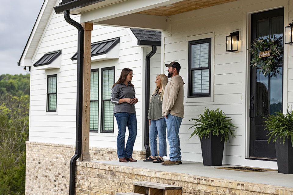 Young couple on the front porch of their new home with Rural 1st loan officer.