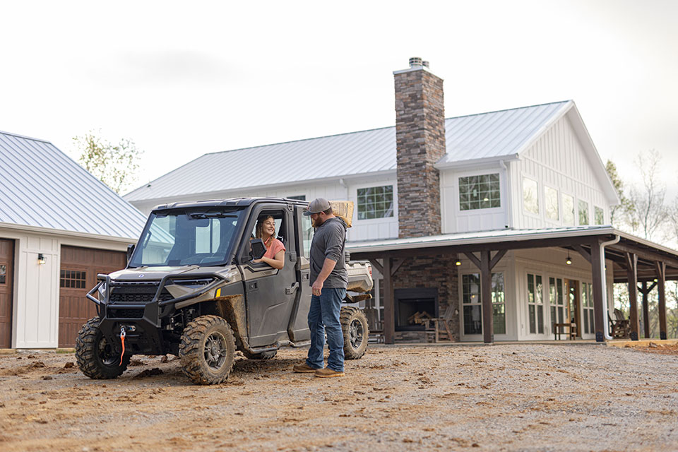 A woman in an ATV talks out the window to a man holding a bag of concrete mix on his shoulder.