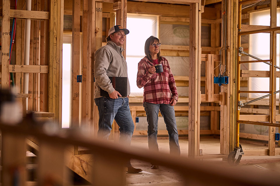 A woman drinking coffee chats with a man holding a folio inside a home being built.
