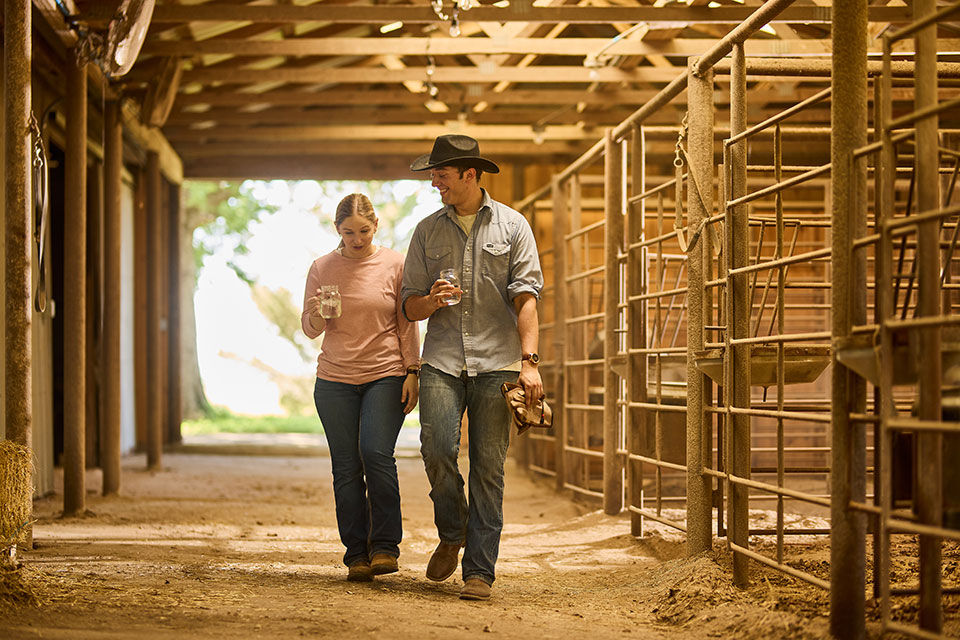 A man in a cowboy hat walks with a woman through a barn.